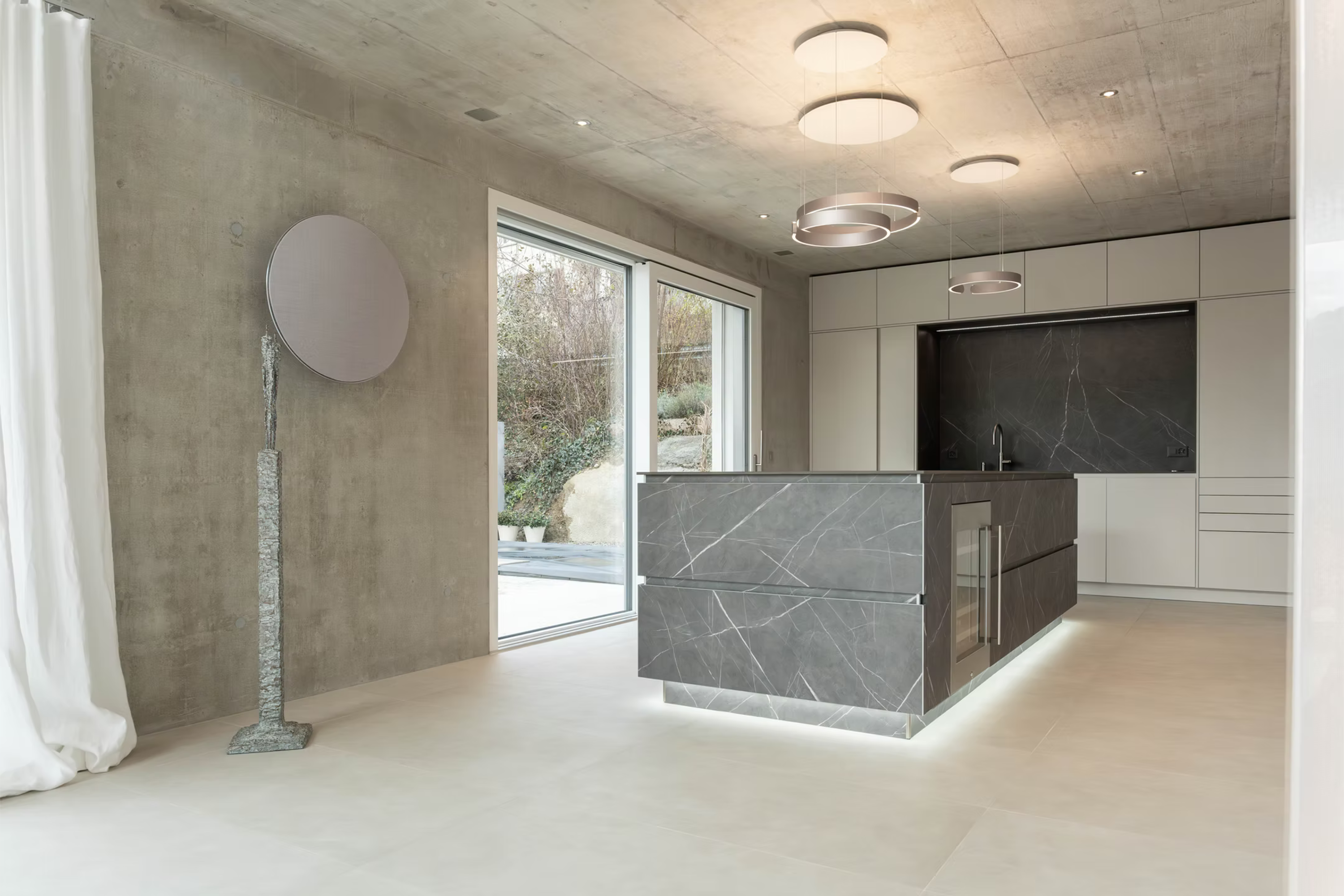 Küche mit grauer Steininsel vor Sichtbetonwand, Weitwinkel